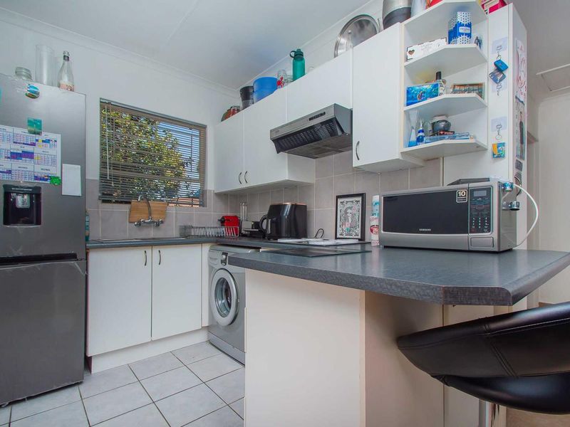 Compact kitchen featuring white cabinetry, dark laminate countertops, tiled backsplash, and integrated laundry plumbing, offering a functional and efficient workspace.