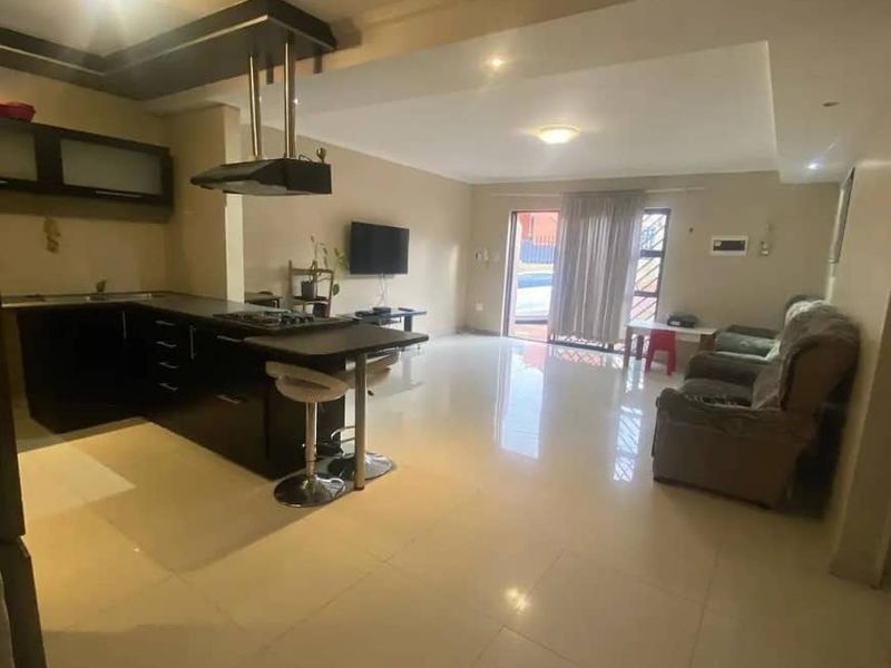 Open-plan living area featuring a modern kitchen with dark cabinetry, gas hob, extractor fan, and tiled flooring leading to a sliding door.