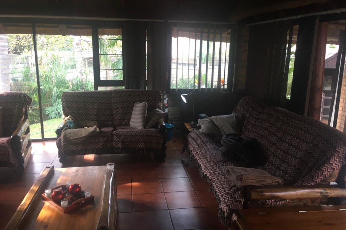 A living room featuring terracotta floor tiles, exposed timber ceiling beams, and large sliding glass doors providing access to the garden.