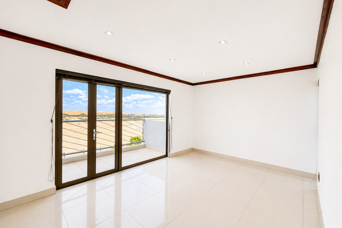 A bright, empty bedroom featuring polished tile flooring, recessed ceiling lighting, dark wood trim, and sliding glass doors opening onto a private balcony with views.