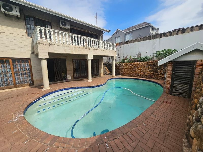 Rear exterior view featuring a swimming pool, paved patio area, and a balcony with balustrades attached to the townhouse structure.