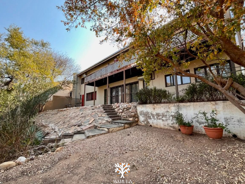 Rear view of the property featuring a stone retaining wall, staircase, and a covered balcony with sliding glass doors.