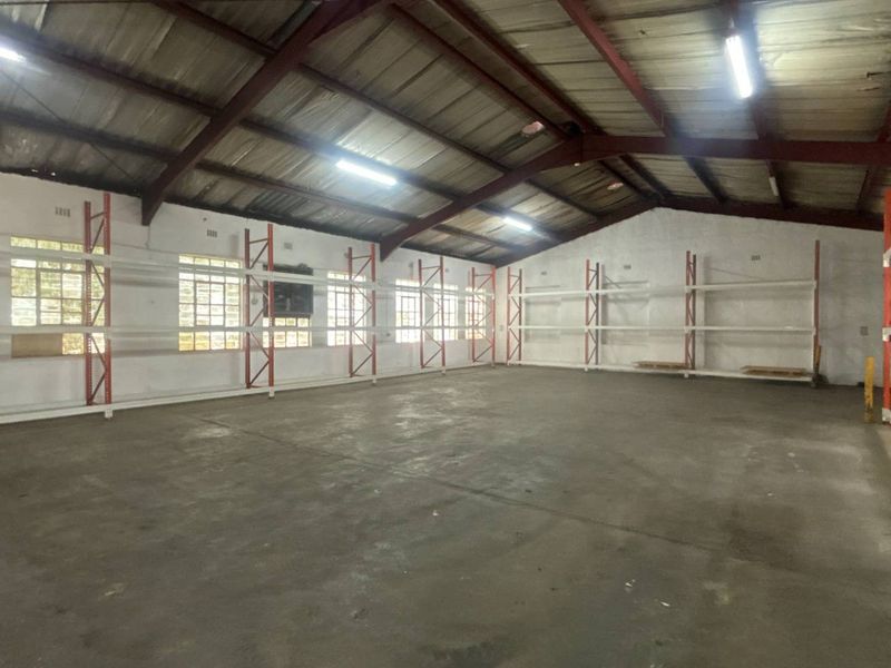 Spacious industrial warehouse unit featuring exposed steel roof trusses, concrete flooring, and integrated metal shelving systems, suitable for storage or light manufacturing operations.