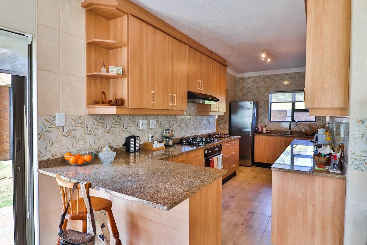Functional kitchen featuring light wood cabinetry, granite countertops, built-in gas hob, extractor fan, and tiled flooring with direct access to the outdoor patio area.