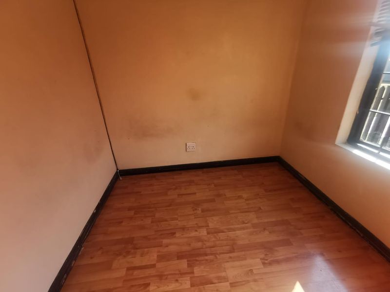 An empty bedroom featuring laminate flooring, a window with security bars, and wall surfaces requiring cosmetic attention.