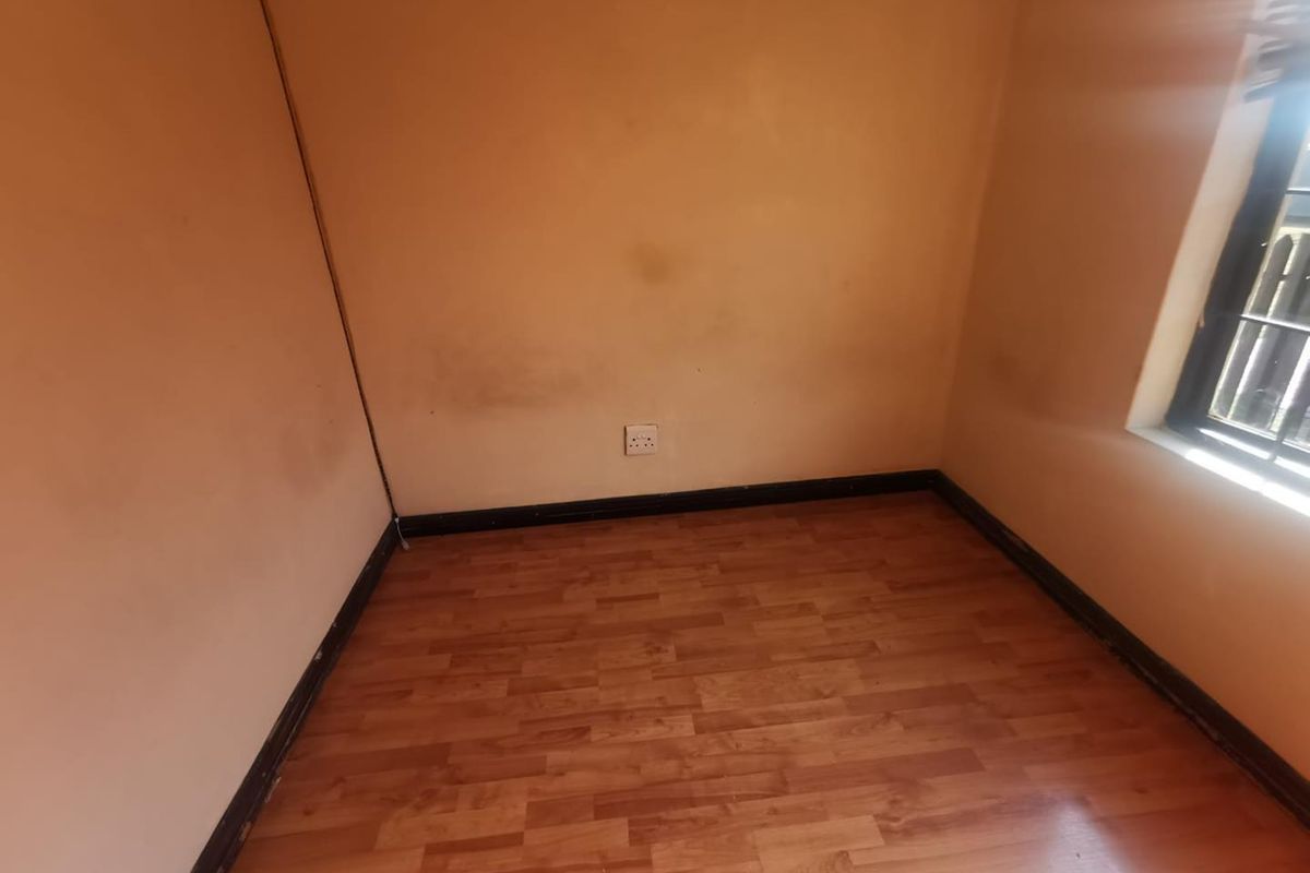 An empty bedroom featuring laminate flooring, a window with security bars, and wall surfaces requiring cosmetic attention.