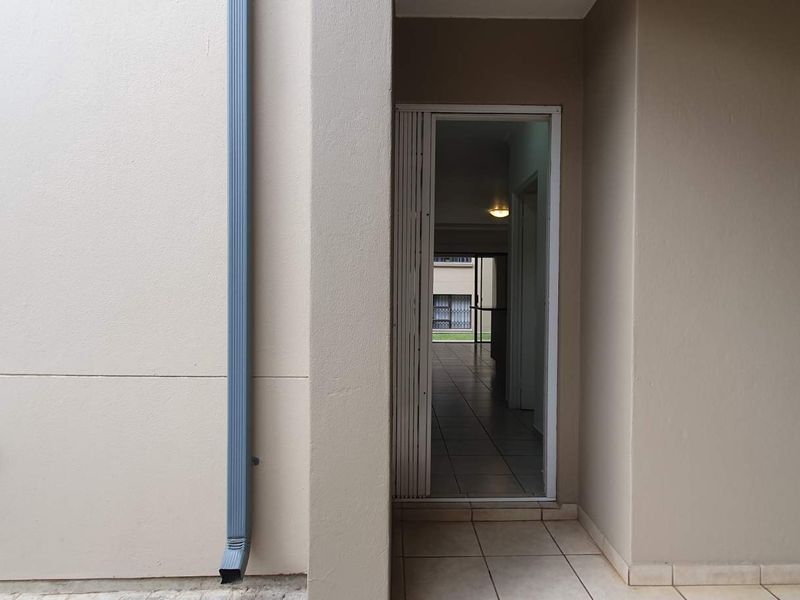 A view of the rear exterior entrance featuring a security gate, tiled patio area, and a downpipe against a neutral-toned wall.