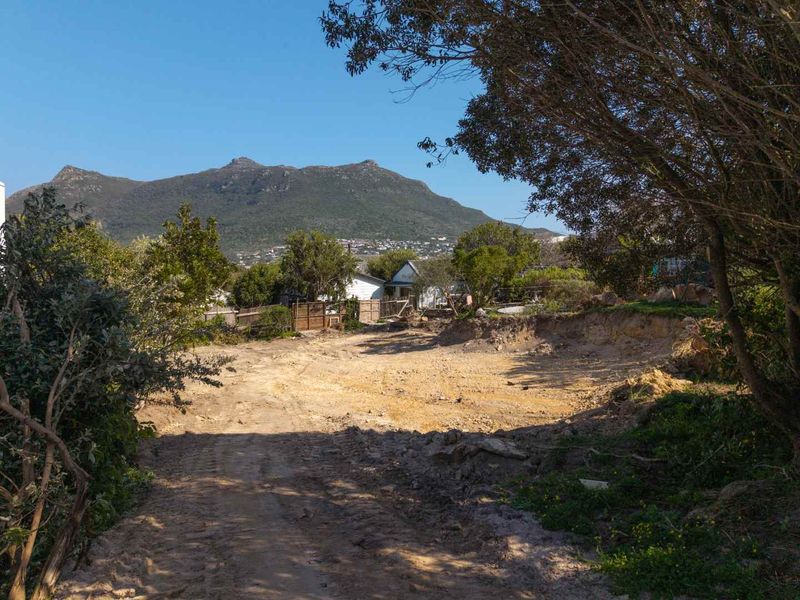 A vacant residential plot featuring cleared ground, mature trees, and scenic mountain views, ready for development.