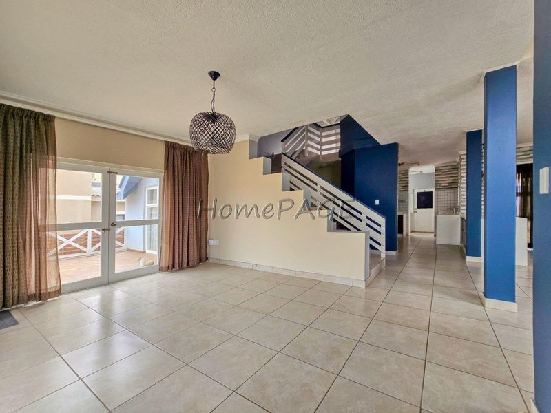 Spacious open-plan living area featuring tiled flooring, a central staircase, and direct access to an outdoor patio through glass sliding doors.