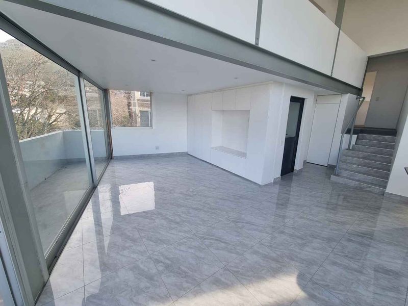 Spacious open-plan living area featuring large format floor tiles, floor-to-ceiling glass doors, built-in cabinetry, and a staircase leading to a mezzanine level.