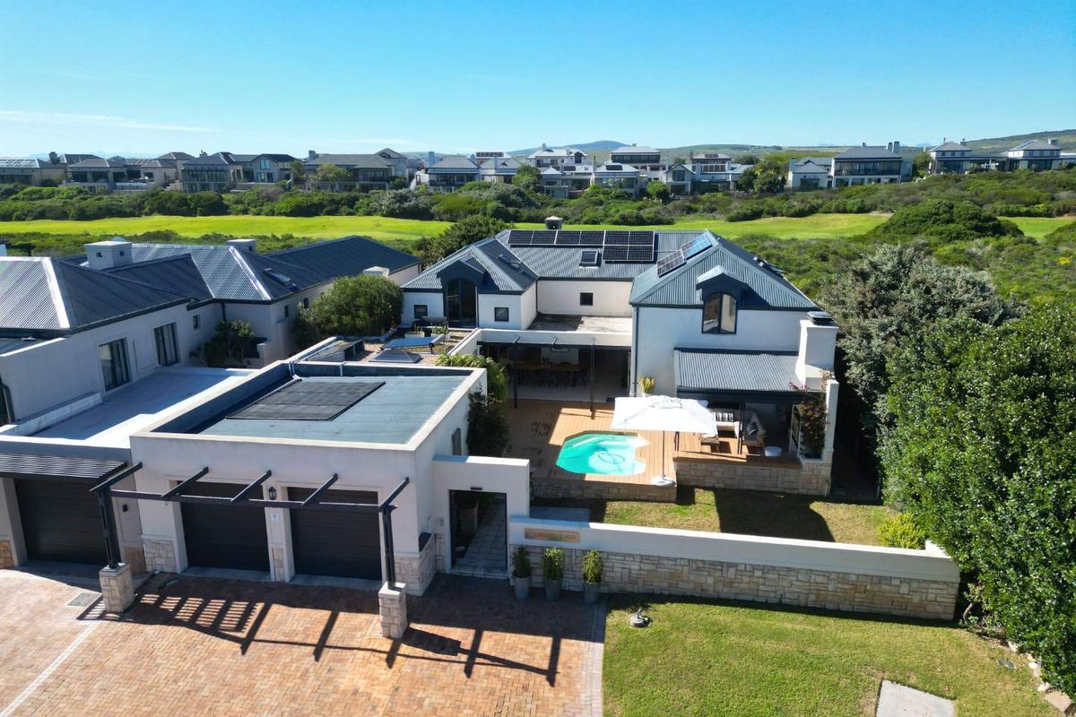 Aerial view of a modern residential property featuring a swimming pool, timber deck, double garage, and solar panels, set within a landscaped estate.