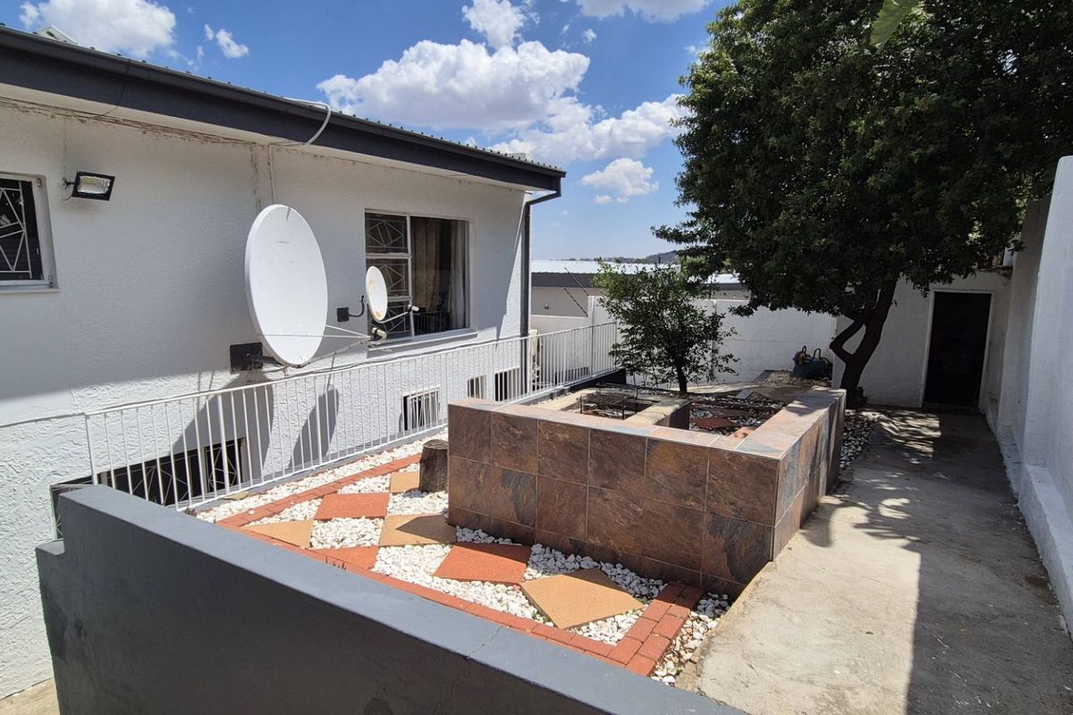 Rear exterior area featuring a tiled built-in braai, concrete paving, and a boundary wall with visible structural cracking.