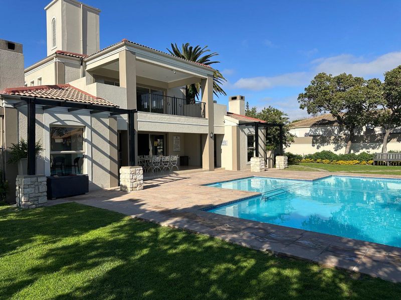 A well-maintained outdoor pool area featuring a swimming pool, stone-clad pillars, a covered patio, and a balcony overlooking the landscaped garden.