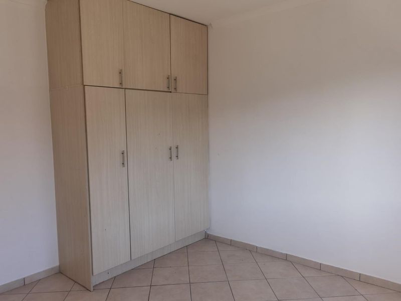 A clean, empty bedroom featuring light wood-finish built-in cupboards and neutral tiled flooring, offering a blank canvas for personalization.