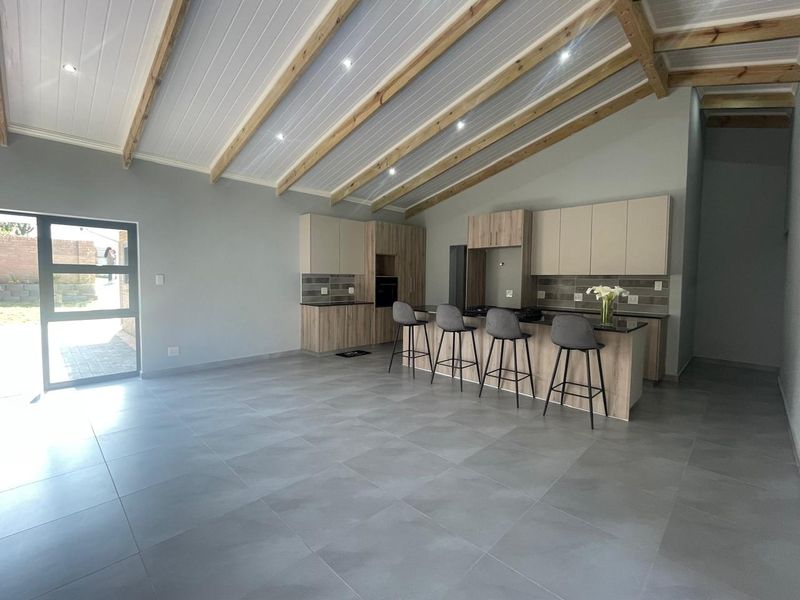 Modern open-plan kitchen and living area featuring high vaulted ceilings with exposed timber beams, sleek cabinetry, a central island, and large glass sliding doors.
