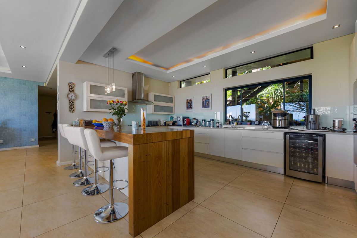 Modern kitchen featuring a large wooden island, sleek white cabinetry, integrated wine cooler, and recessed ceiling lighting with a contemporary open-plan layout.