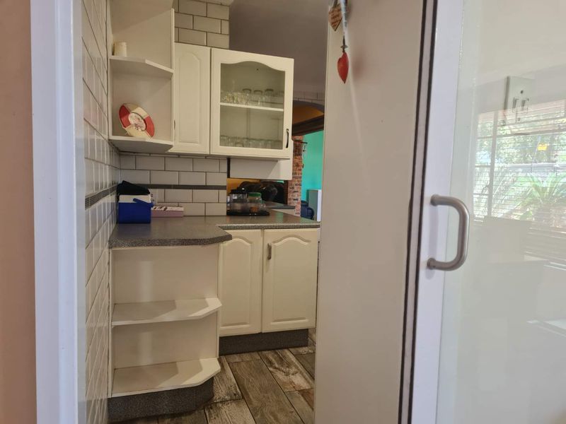 A functional scullery area featuring white cabinetry, subway tile backsplash, laminate countertops, and durable wood-look tile flooring, providing additional storage and prep space.