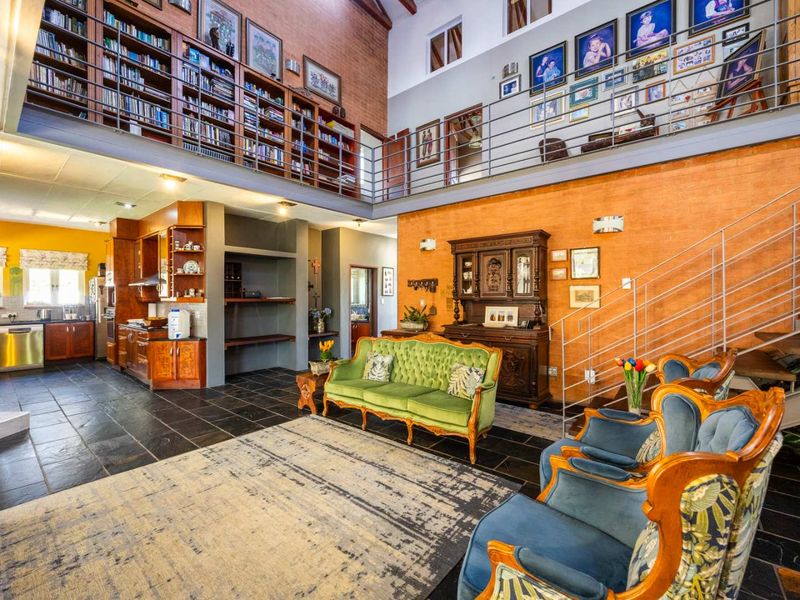 Spacious open-plan living area featuring a double-volume ceiling, mezzanine library, slate flooring, and an integrated kitchen with warm wood cabinetry.