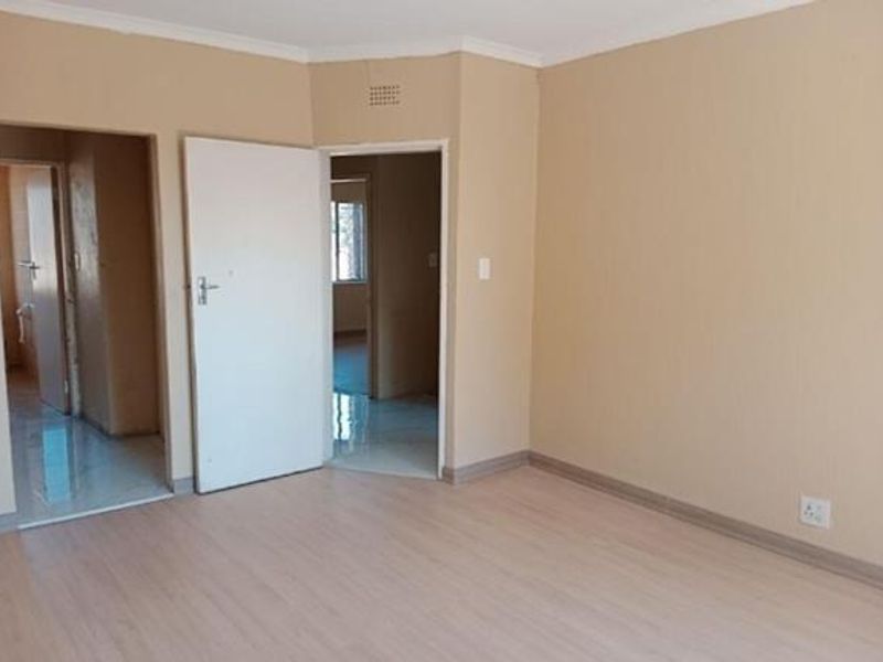 An empty living room featuring light-toned laminate flooring, neutral wall paint, and coved cornicing, providing a clean and versatile space for interior design.
