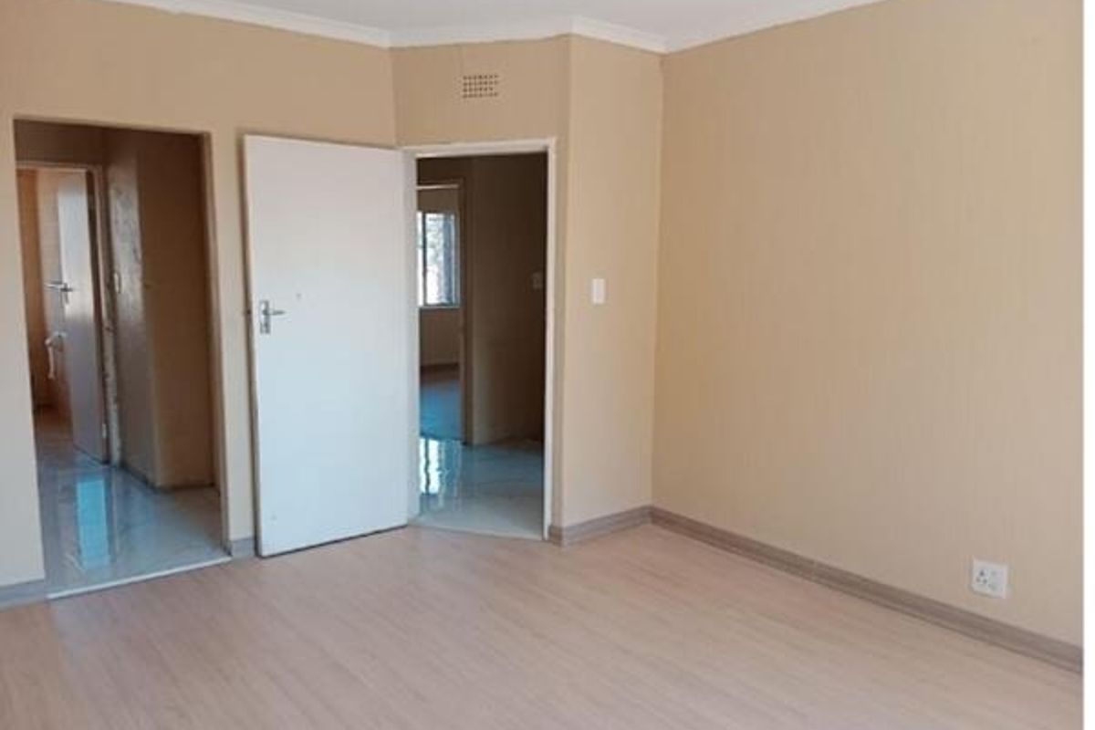 An empty living room featuring light-toned laminate flooring, neutral wall paint, and coved cornicing, providing a clean and versatile space for interior design.