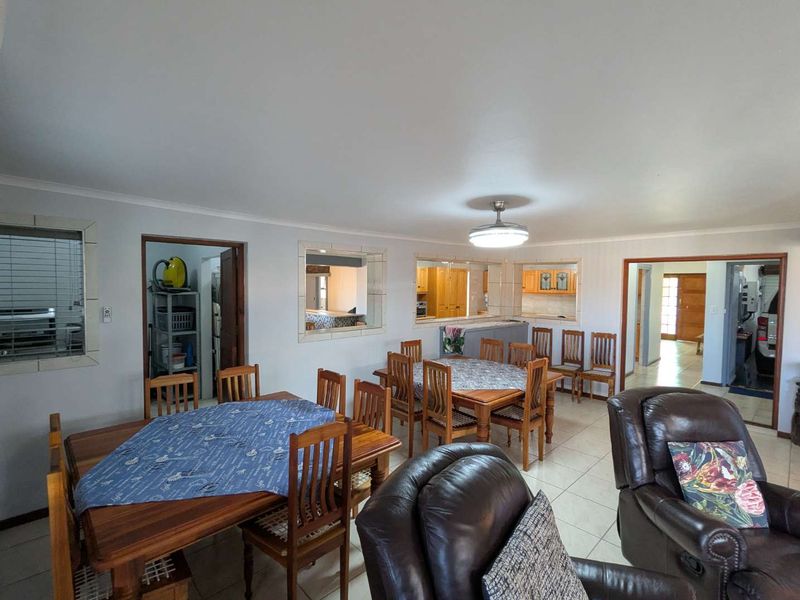 Spacious open-plan living and dining area featuring tiled flooring, a ceiling fan, and convenient pass-through windows connecting to the kitchen.