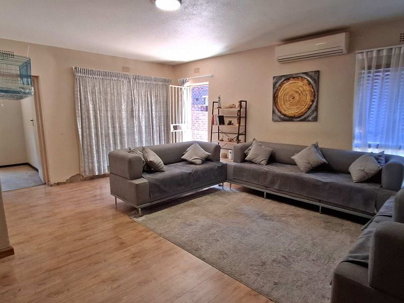A spacious living room featuring laminate flooring, a wall-mounted air conditioning unit, and direct access to an outdoor area through a security gate.