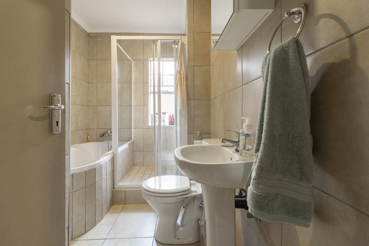 A functional bathroom featuring a pedestal basin, a built-in bathtub, and a separate glass-enclosed shower stall with neutral wall and floor tiling.
