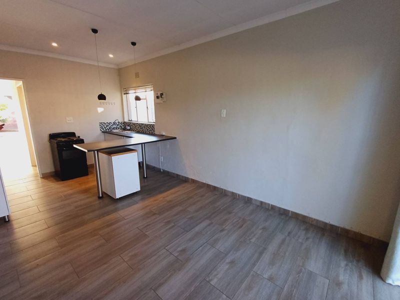 An open-plan living and kitchen area featuring wood-look tiled flooring, a breakfast bar, and a functional kitchen layout with a freestanding stove.