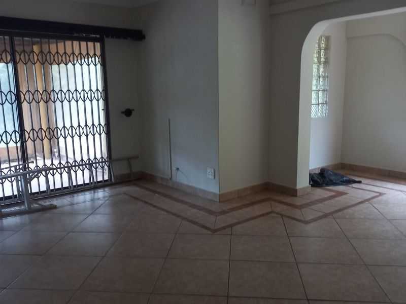 An empty living area featuring ceramic tile flooring, a security gate, and an arched entryway leading to an adjacent space with glass block windows.