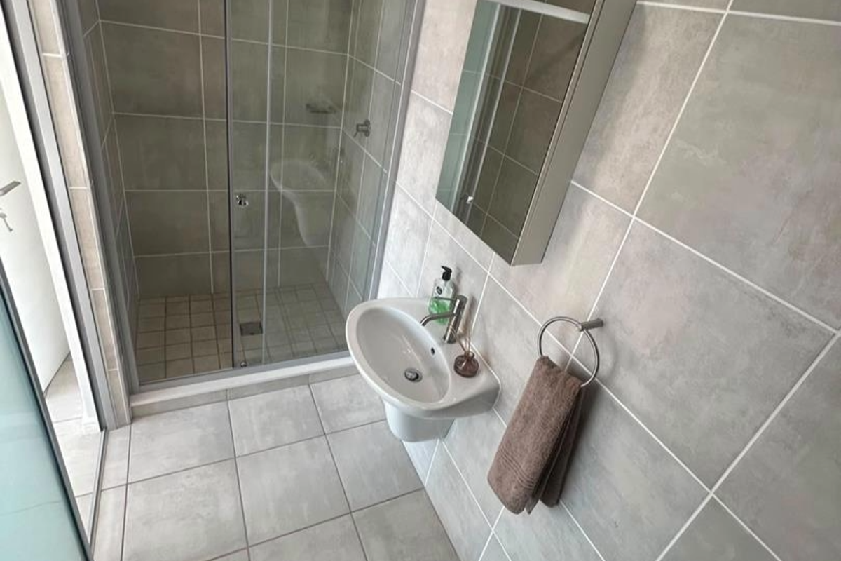 Modern bathroom featuring a glass shower enclosure, wall-mounted basin, and a mirrored medicine cabinet with neutral grey tiling throughout.