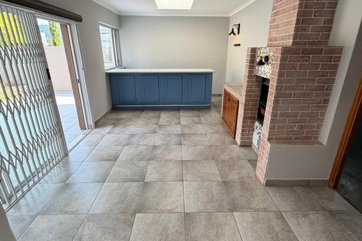 Spacious entertainment area featuring a built-in brick fireplace, blue cabinetry, tiled flooring, and sliding glass doors leading to the outdoor patio.