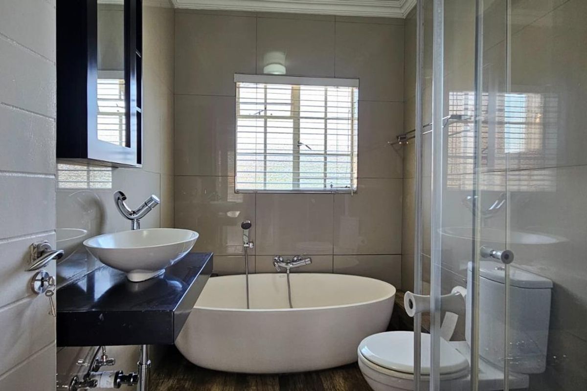 Modern bathroom featuring a freestanding bathtub, vessel sink on a floating vanity, and a glass-enclosed shower with neutral wall tiling.