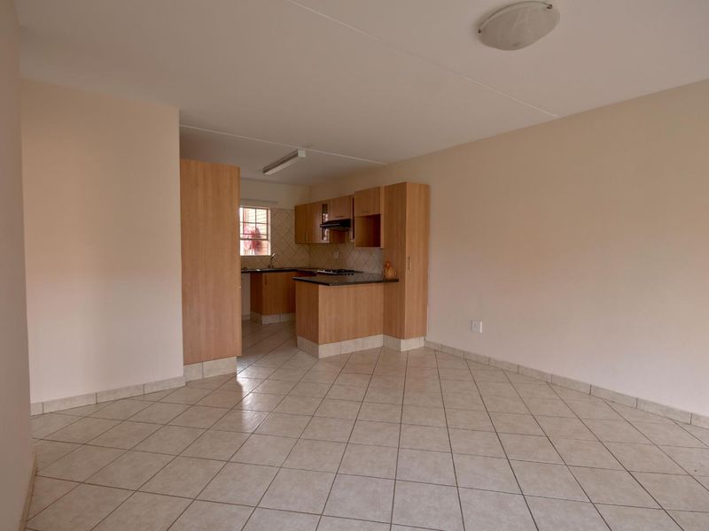An open-plan living and kitchen area featuring neutral tiled flooring, light wood cabinetry, and granite countertops in a clean, vacant space.