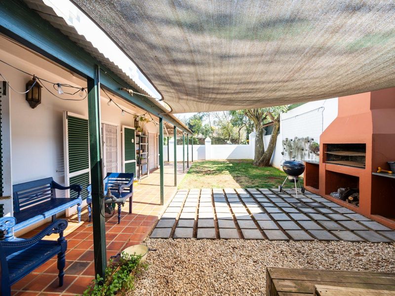 Covered outdoor patio featuring a built-in braai, shade sail, and tiled flooring, leading out to a private garden area.