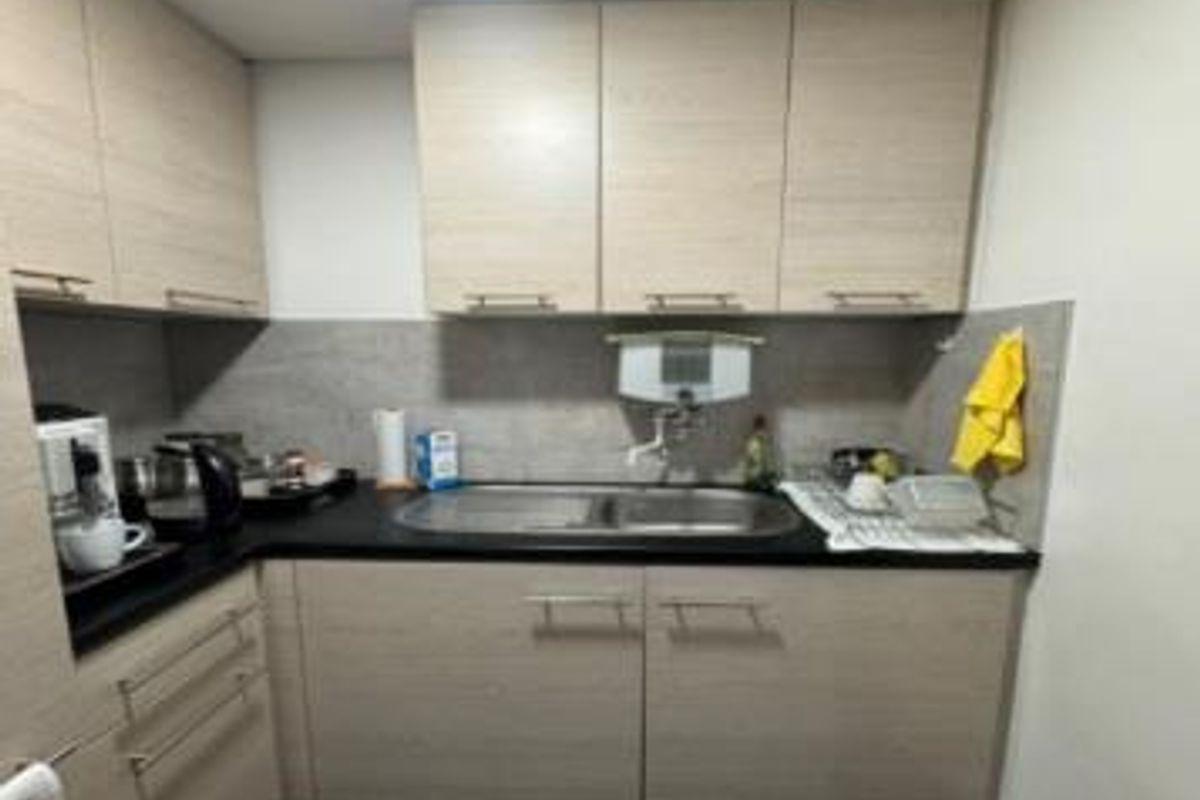 Compact kitchen area featuring light wood-tone cabinetry, dark countertops, a stainless steel double sink, and a tiled backsplash.