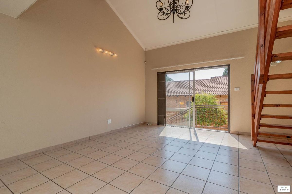 Spacious living area featuring vaulted ceilings, tiled flooring, and a wooden staircase, with direct access to an outdoor balcony through sliding glass doors.