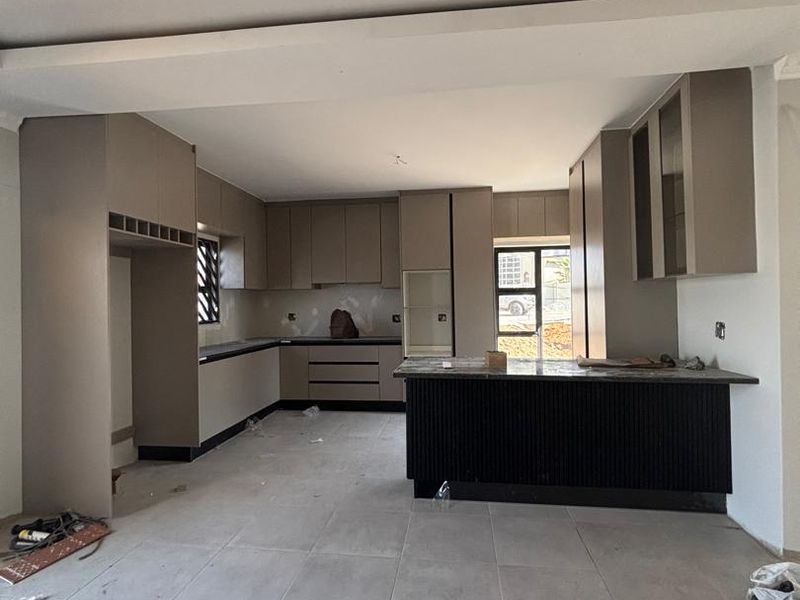 A modern, unfinished kitchen featuring neutral cabinetry, a central island with stone countertops, and large format floor tiles, currently in the final stages of construction.