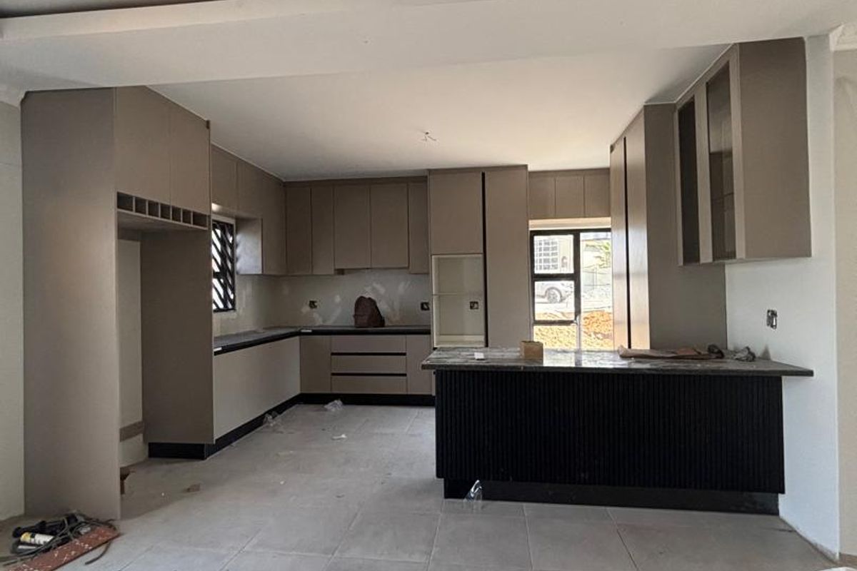 A modern, unfinished kitchen featuring neutral cabinetry, a central island with stone countertops, and large format floor tiles, currently in the final stages of construction.