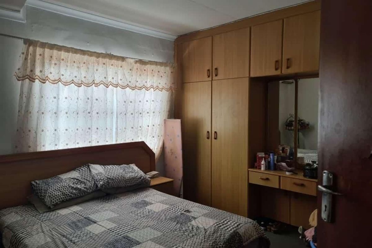A bedroom featuring built-in wooden cupboards and a vanity unit, requiring cosmetic updates to the ceiling and wall finishes.