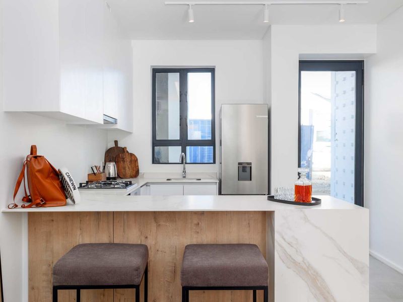 Modern kitchen featuring sleek white cabinetry, stone countertops, a breakfast bar, and integrated gas hob, offering a clean and functional culinary space.