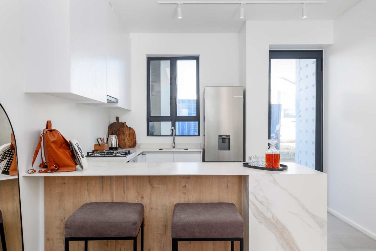 Modern kitchen featuring sleek white cabinetry, stone countertops, a breakfast bar, and integrated gas hob, offering a clean and functional culinary space.