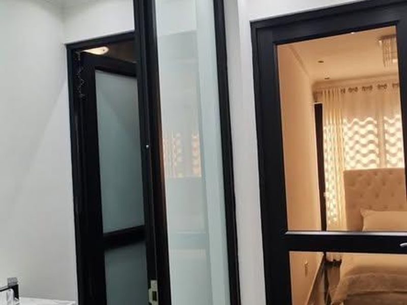 A modern hallway featuring sleek black-framed glass doors, marble-look floor tiles, and recessed downlighting, providing a clean and contemporary transition between rooms.