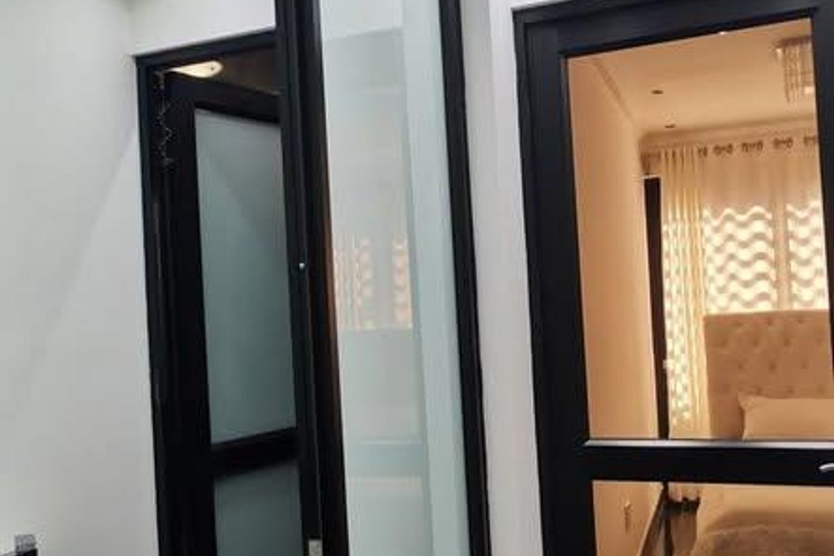 A modern hallway featuring sleek black-framed glass doors, marble-look floor tiles, and recessed downlighting, providing a clean and contemporary transition between rooms.