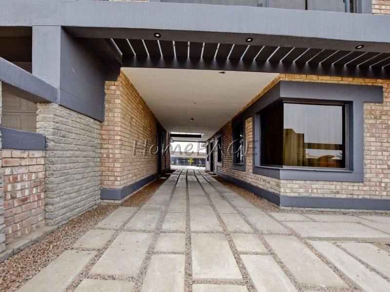 A modern exterior entrance featuring a brick facade, concrete driveway, and a covered pergola area with recessed lighting.