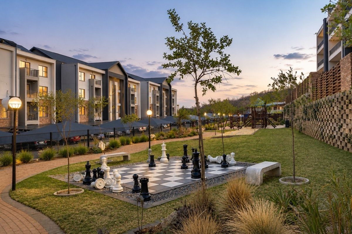 A well-maintained communal garden area featuring a large outdoor chess set, paved walkways, concrete seating, and landscaped grounds within an apartment complex.