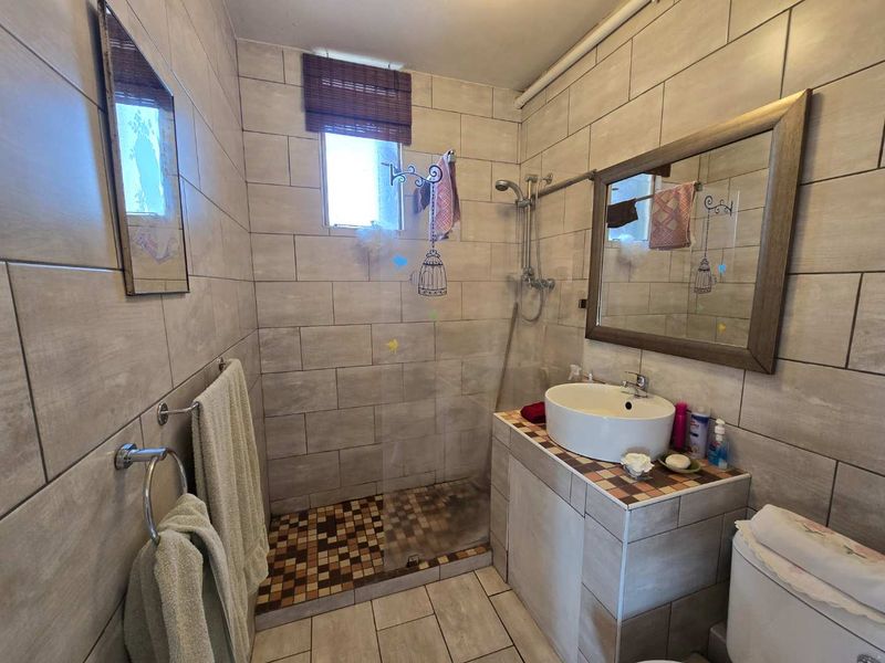 A functional bathroom featuring a tiled shower enclosure, vessel sink vanity, and neutral wall tiling throughout.