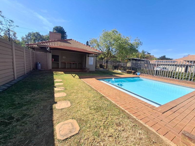 Outdoor entertainment area featuring a swimming pool with brick coping, a covered patio with a built-in braai, and a private garden space.