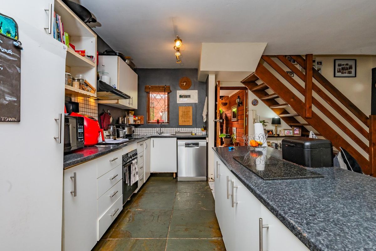 Functional kitchen featuring built-in cabinetry, stone tile flooring, and a central island, adjacent to an open staircase in this townhouse setting.