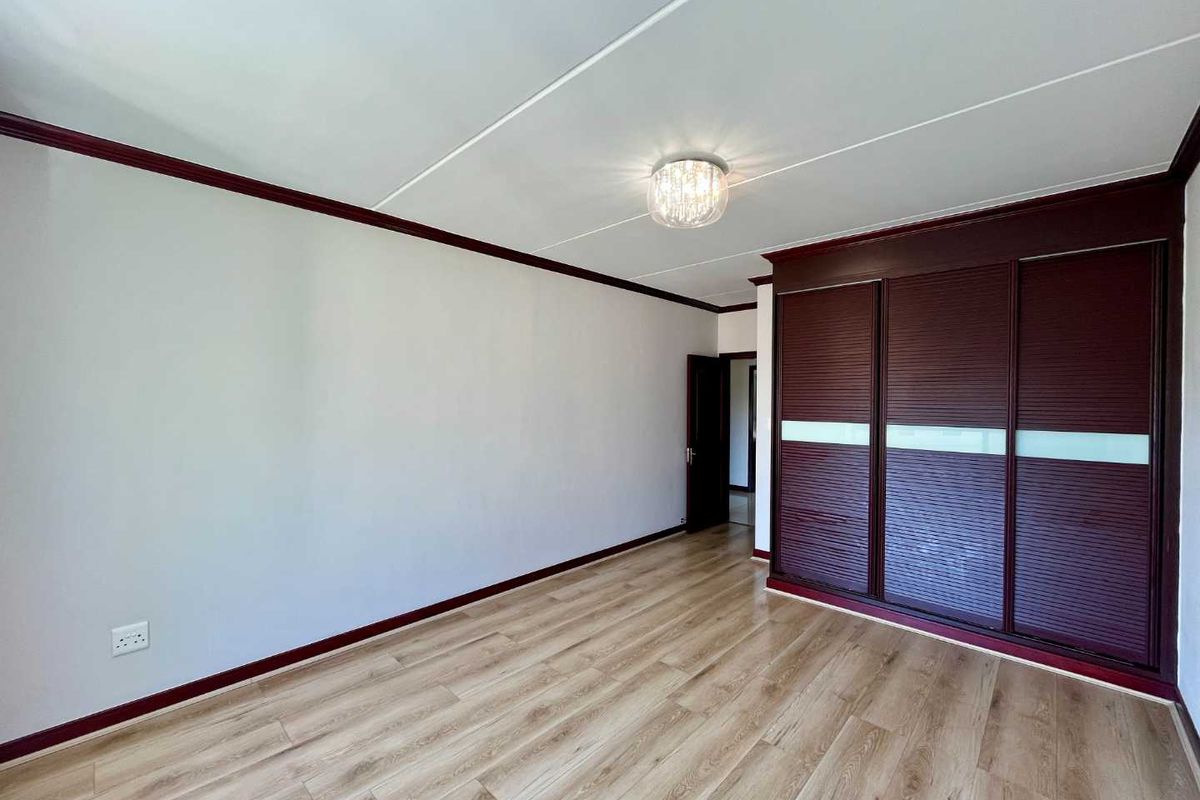 A bright bedroom featuring wood-look laminate flooring, dark wood-toned built-in sliding door wardrobes, and decorative crown molding.
