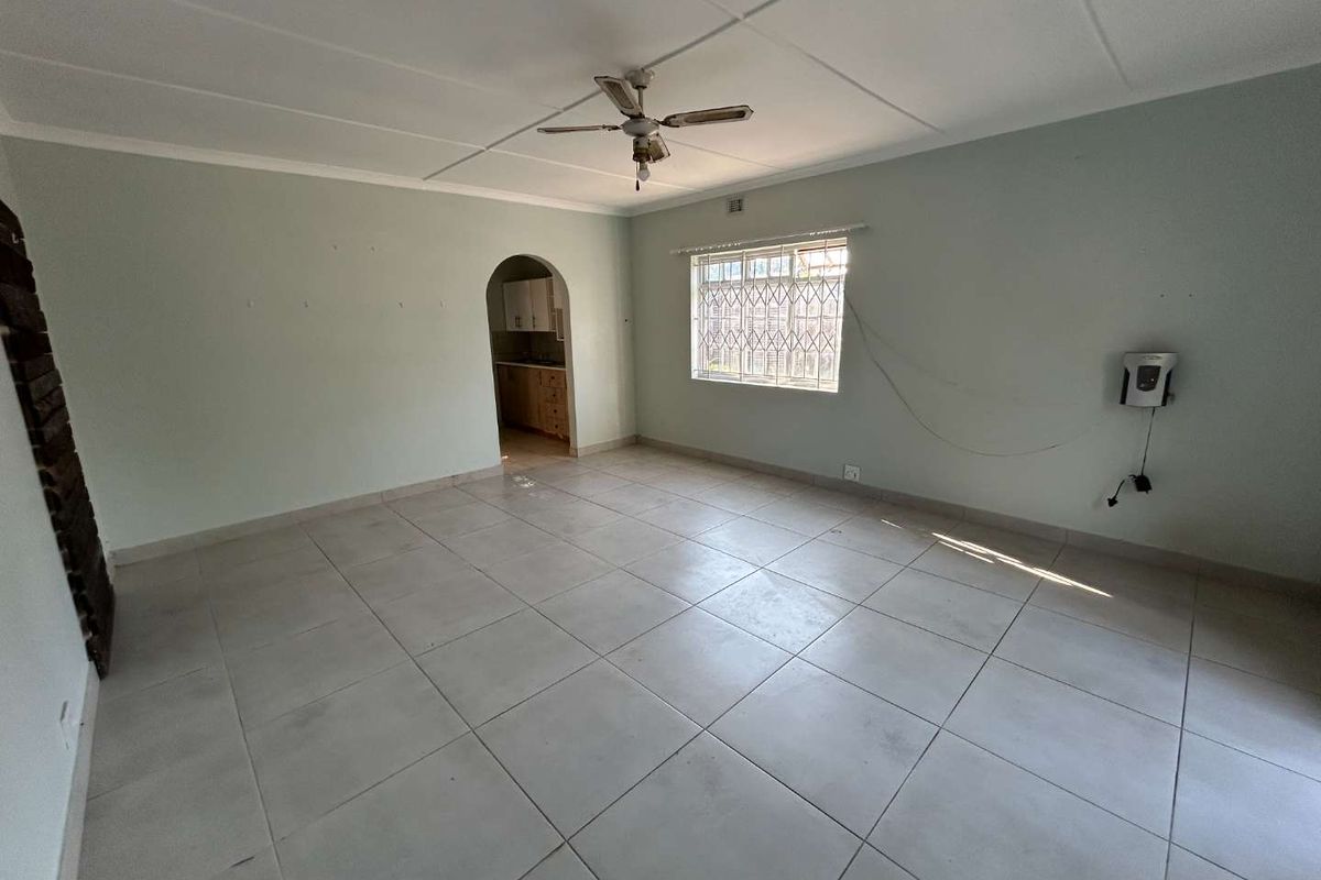 Spacious, empty living area featuring neutral tiled flooring, a ceiling fan, and an arched entryway leading to the kitchen.